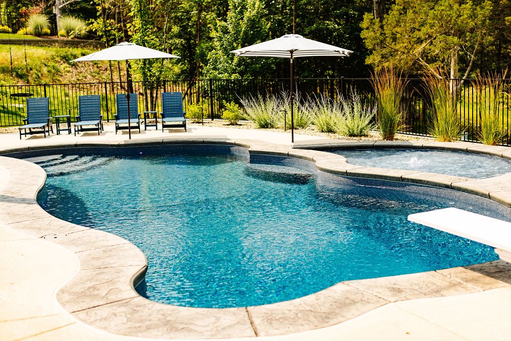 freeform fiberglass pool with tanning ledge, nice landscaping and safety fence